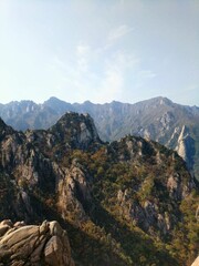 Vertical view from a steep cliff to a mountain range, dense forests on a sunny day