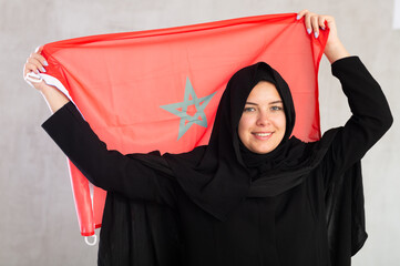 Smiling joyful Muslim woman in traditional black hijab holding Moroccan flag. Portrait of Muslim...