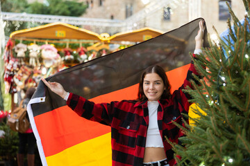 Cheerful young girl holding national flag of Germany, standing outdoors against blurred background...