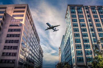Low angle shot of passenger plane flies over city buildings under blue cloudy sky