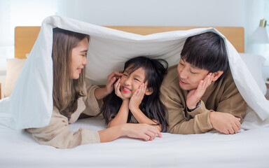 Three people of Asian family, father, mother, little daughter laying down under or covered by...