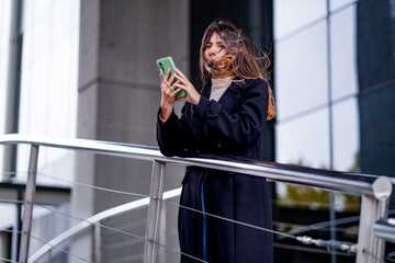 Caucasian woman talks on cell phone and sends messages with corporate building in the background.