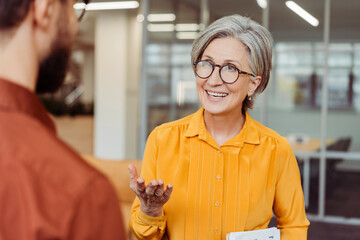 Portrait of smiling confident senior woman wearing eyeglasses communication with colleague at...