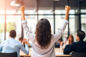 Rear view of a casual businesswoman raising her arms in a full conference room waiting for her turn to speak up