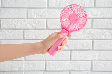 Hand of young woman with mini fan on white brick background