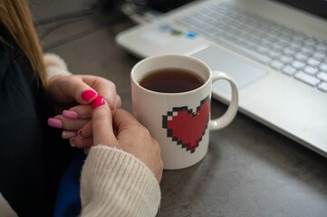 Closeup shot of the woman's hands near the pixel heart mug and a laptop