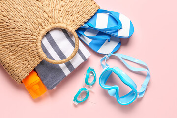 Female bag with beach accessories and bottle of sunscreen cream on color background