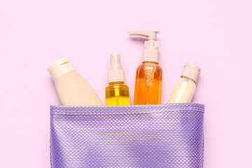 Bag with set of travel cosmetic products on lilac background