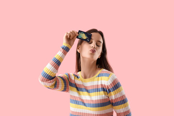 Young woman with credit card blowing kiss on pink background