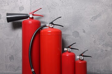 Four red fire extinguishers near grey wall