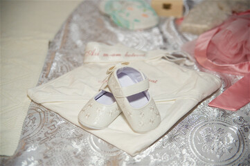 Pair of white baby shoes placed on a tablecloth with patterns