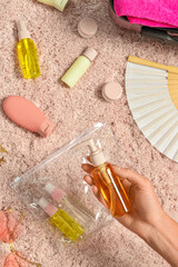 Female hand with travel cosmetics kit and accessories on fabric background