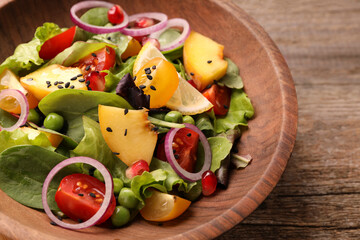 Delicious salad with peach, green peas and vegetables in bowl on wooden table, closeup