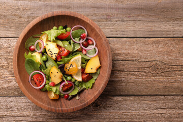 Delicious salad with peach, green peas and vegetables in bowl on wooden table, top view. Space for text