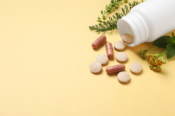 Different pills and herbs on light yellow background, space for text. Dietary supplements