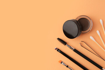 Eyebrow pomade with henna effect and professional tools on orange background, flat lay. Space for...