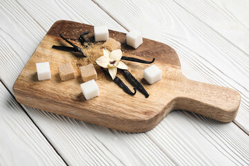 Fototapeta na wymiar Board with aromatic vanilla sugar, flower and sticks on white wooden background