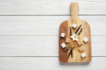 Board with aromatic vanilla sugar, flower and sticks on white wooden background