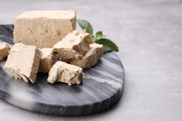 Fototapeta premium Pieces of tasty halva and mint served on light grey table, closeup. Space for text