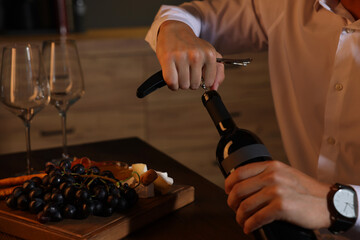 Romantic dinner. Man opening wine bottle with corkscrew at table indoors, closeup