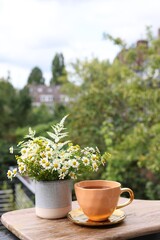 Cup of delicious chamomile tea and fresh flowers outdoors