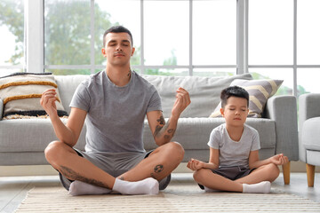 Young man with his little son meditating at home - obrazy, fototapety, plakaty