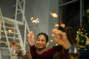 happy female and friends holding sparkler fireworks in a party with Christmas tree. young Asian...