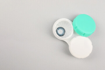 Case with blue contact lenses on light grey background, top view. Space for text