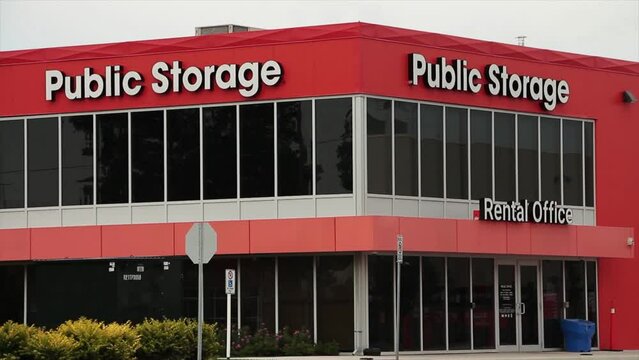 storage building public storage in white writing on orange background with dark windows with traffic passing on road in foreground, tight on corner of building with caption
