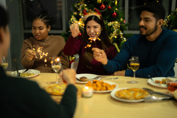 happy female and friends holding sparkler fireworks in a party with Christmas tree. young Asian people enjoy celebrating Christmas and New Year. celebrate with food wine and friendship for love,