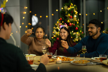 happy female and friends holding sparkler fireworks in a party with Christmas tree. young Asian people enjoy celebrating Christmas and New Year. celebrate with food wine and friendship for love,