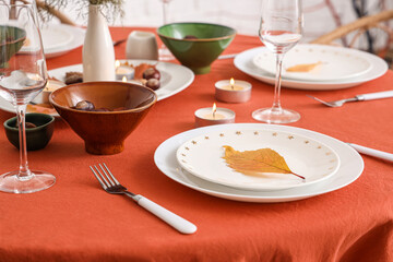 Autumn table setting with burning candles and dry leaves, closeup
