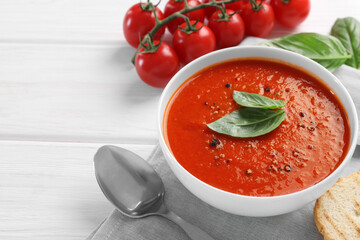 Delicious tomato cream soup in bowl on white wooden table, space for text