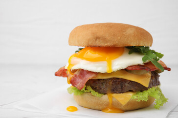 Delicious burger with fried egg on white table, closeup. Space for text