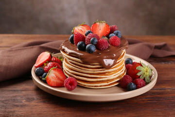 Stack of tasty pancakes with fresh berries and chocolate spread on wooden table - obrazy, fototapety, plakaty