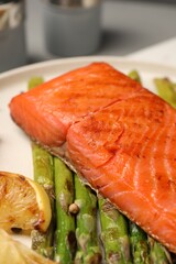 Tasty grilled salmon with asparagus, tomatoes and lemon on plate, closeup
