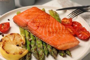 Tasty grilled salmon with asparagus, tomatoes and lemon on plate, closeup
