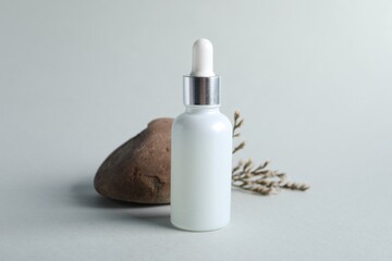 Bottle with cosmetic serum, stone and dry flowers on light grey background