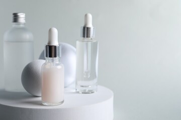Fototapeta na wymiar Stylish presentation of bottles with cosmetic serums on light grey background, space for text