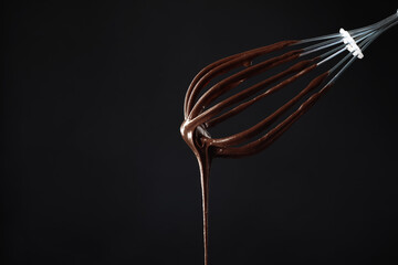 Chocolate cream flowing from whisk on black background, closeup. Space for text