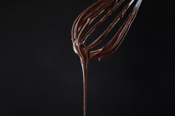 Chocolate cream flowing from whisk on black background, closeup
