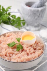 Fototapeta na wymiar Fresh raw minced meat, parsley and egg in bowl on light grey table, closeup