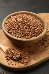 Bowl and spoon with dry buckwheat on black table, closeup