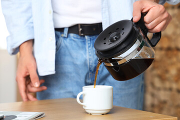 Fototapeta na wymiar Handsome young man pouring hot espresso from coffee pot into cup in office, closeup