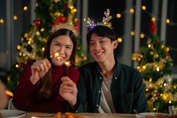 man and woman holding sparkler fireworks in a party with Christmas tree. young couple Asian people...