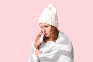 Ill young woman with nasal drops on pink background