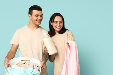 Young couple with laundry basket and bottle of detergent on blue background