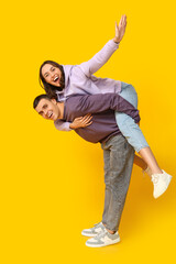 Happy young man giving piggyback ride to his girlfriend on yellow background