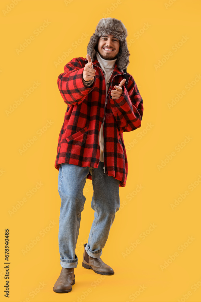 Canvas Prints Young man in winter clothes pointing at viewer on yellow background