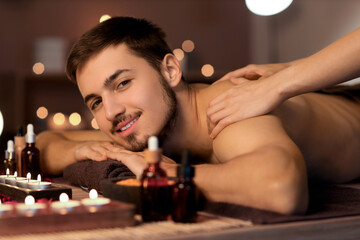 Young man getting massage in dark spa salon, closeup